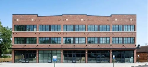 Brick exterior of a modern three-story apartment building with large industrial-style windows.
