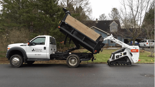small white company dump truck with bobcat loading soil