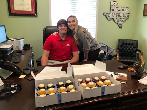 Agent Samuel and wife standing and smiling together in office with sweet treat