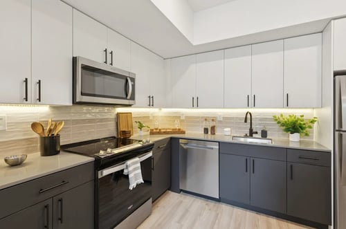 The contemporary two-tone kitchen at The Gio Apartments in Philadelphia, PA, features modern gray cabinets, stainless steel appliances, and a unique textured subway tile backsplash.