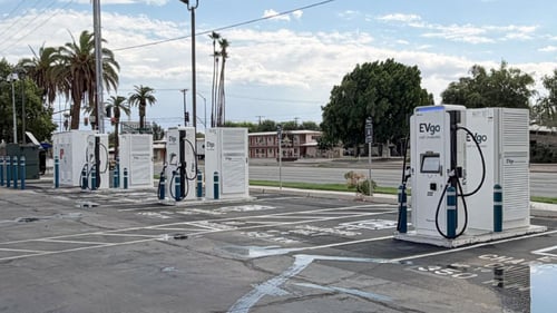 Several EVgo fast charging units installed in marked parking spaces at a public charging station, with EVgo logos on the chargers, protective bollards around each unit