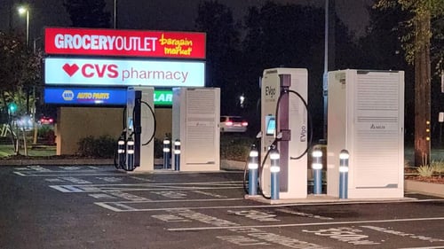 Several EVgo fast-charging units installed in marked parking spaces at a public charging station, with EVgo logos on the chargers, protective bollards around each unit