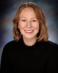 Emily Norman, APRN, CNP smiling in front of a gray background.