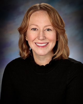 Emily Norman, APRN, CNP smiling in front of a gray background.