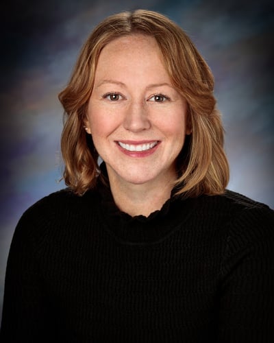 Emily Norman, APRN, CNP smiling in front of a gray background.