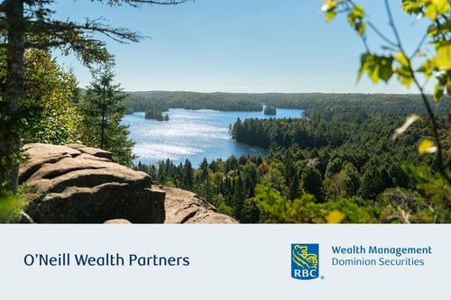 Forested lake with blue water, surrounded by green trees and rocky outcrop. O'Neill Wealth Partners.