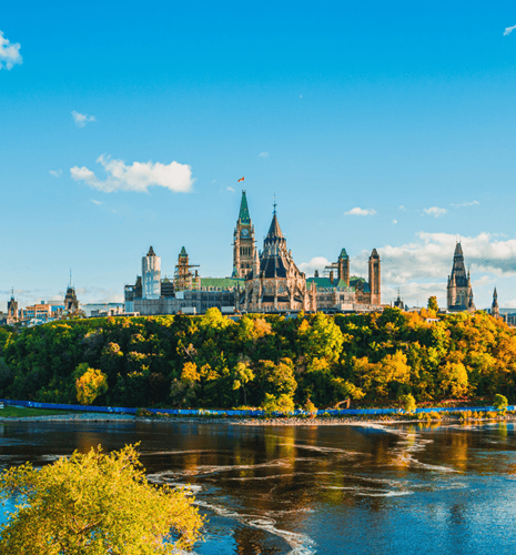 Parliament Hill surrounded by fall foliage and the Ottawa River.