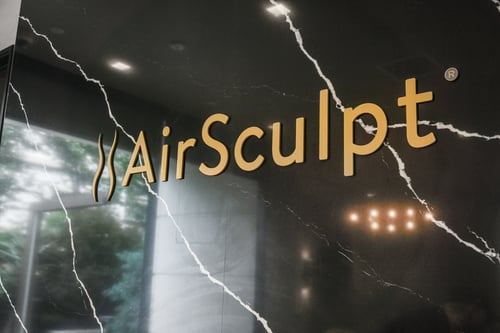 Image of an AirSculpt Logo - yellow text against a black marble background with cracked white lines