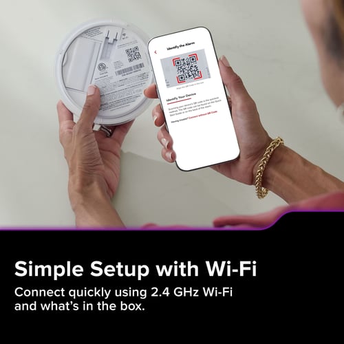 A person connects their app to their new smart alarm by scanning the QR code on the back. The text below reads "Simple Setup with Wi-Fi, Connect quickly using 2.4 GHz Wi-Fi and what's in the box."