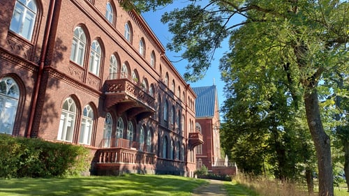 Punatiilinen suuri rakennus, puita ja vihreää nurmikkoa.