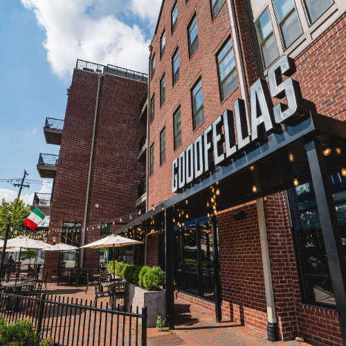 Exterior view of Goodfellas Pizzeria on Baxter Avenue with outdoor patio seating and Italian flag.