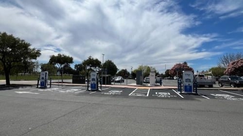 Several EVgo fast charging units installed in marked parking spaces at a public charging station, with EVgo logos on the chargers, protective bollards around each unit