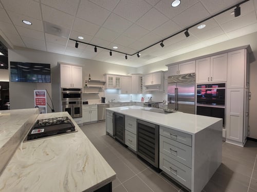 Kitchen appliance showroom with a gray kitchen island on display surrounded by white cabinets and stainless steel appliances