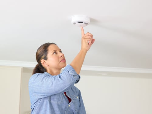 A woman pushes the test button on her smoke alarm.