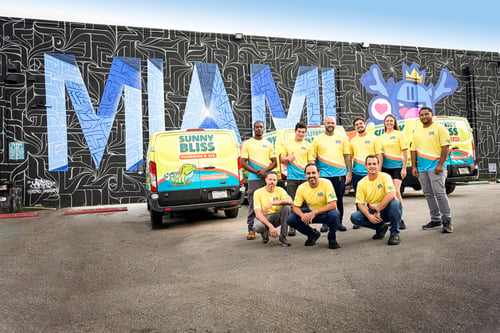 Sunny Bliss Plumbing & Air Team in front of wrapped vehicles and Miami background