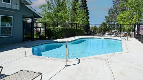 a pool with a fence around it and a house in the background at Sierra Oaks Living Apartments, Cameron Park, California