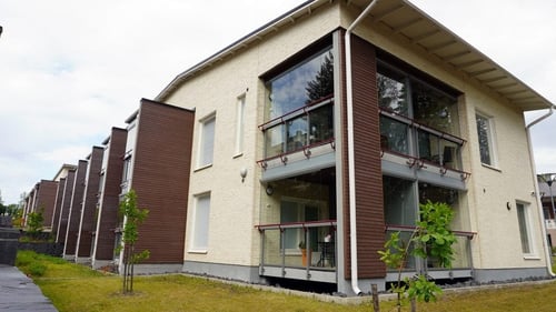 Ulkokuva Lastutieltä. Rakennus on vaalean sävyinen ja siinä on tummapuisia yksityiskohtia. Taloa ympäröi nurmikko, jolle on istutettu puuntaimia.