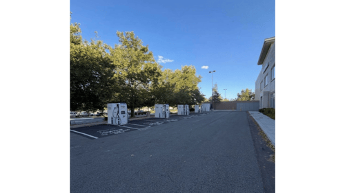 Several EVgo fast charging units installed in marked parking spaces at a public charging station, with EVgo logos on the chargers, protective bollards around each unit.