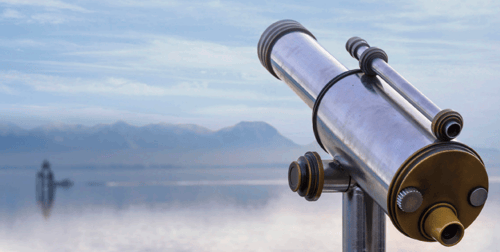 A silver telescope on a stand points towards a calm sea with a distant boat and mountain range under a cloudy sky, evoking a sense of exploration.
