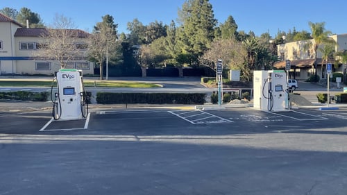 Several EVgo fast-charging units installed in marked parking spaces at a public charging station, with EVgo logos on the chargers, protective bollards around each unit