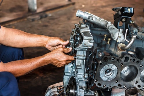 A person uses tools to work on a disassembled car engine, adjusting parts and bolts in a workshop setting.