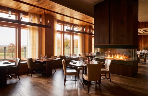 Dining room with wood interiors and large windows overlooking forest views.