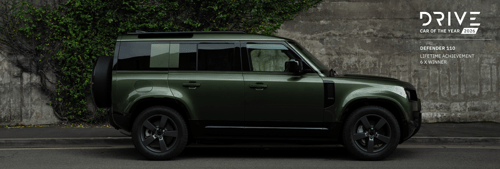 Pangea Green Defender 110 parked beside a reflective water surface in a misty rainforest