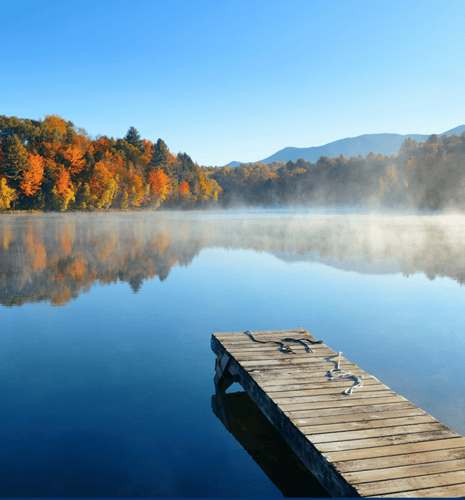 A wooden dock and a calm lake surrounded by fall foliage.