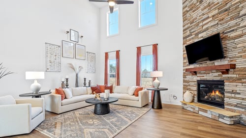 Family room with cathedral ceiling, couch and chair seating area and stone fireplace at DRB Homes The Grange community
