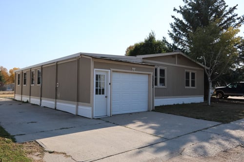 An exterior view of a beige mobile home and a beige garage that has a white door.