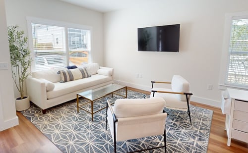 The stylish apartment living room at Belle Meadow Asheville features a white sofa set, a prominent patterned area rug, and a wall-mounted flat-screen TV.