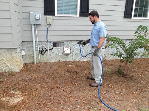 Pest control technician applying treatment around a home foundation for termite prevention