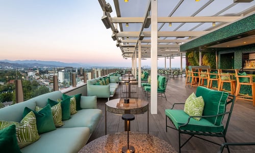Rooftop patio, tables, mood lighting, outdoor bar area, views of Beverly Hills and California mountains.