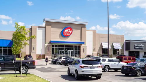 White SUV driving through crowded parking lot of 24 Hour Fitness