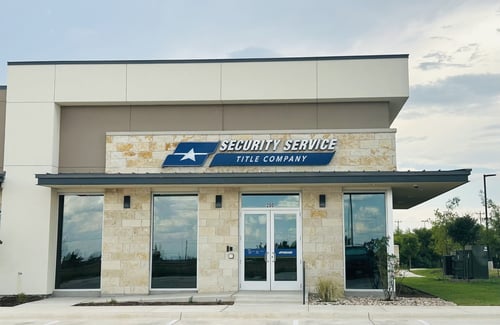 Front exterior of Security Service Title Company building in Kyle, TX, viewed from the parking lot, featuring stone facade, glass double doors and clear signage.