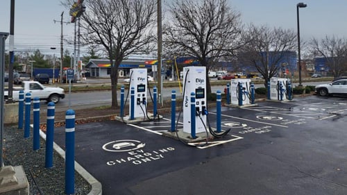 Several EVgo fast charging units installed in marked parking spaces at a public charging station, with EVgo logos on the chargers, protective bollards around each unit.