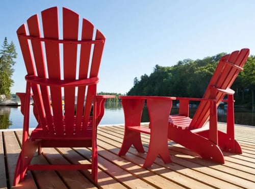 Two red Muskoka chairs overlooking a lake.