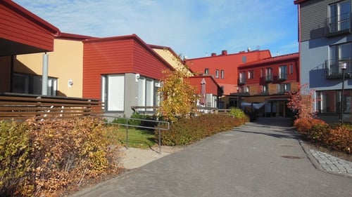Ulkokuva Nyyttipuistosta. Rakennukset ovat punaisia ja tie on asfaltoitu. Pihapiirissä on syksyn väreissä komeilevia pensaita ja nuoria puita.