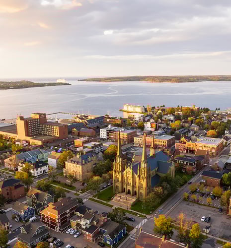 Aerial view of a coastal city at sunset, featuring a prominent cathedral with twin spires, surrounded by historic buildings and a serene waterfront.