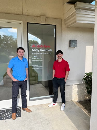 Two team members standing and smiling outside of agency door wearing red and blue shirts with jeans