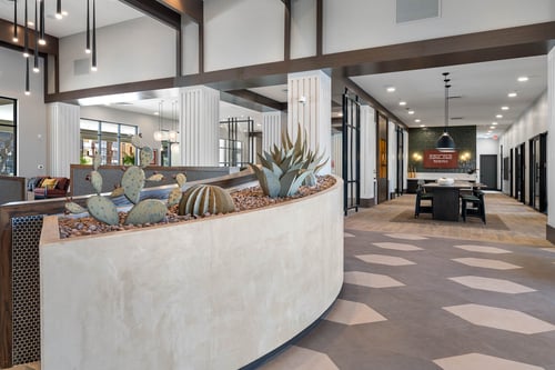 Lobby entry area with a curved planter featuring cacti and agave, surrounded by geometric tile flooring and modern decor accents.