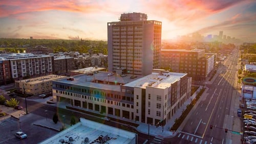 A cityscape with a large building in the foreground and a sunset in the background.