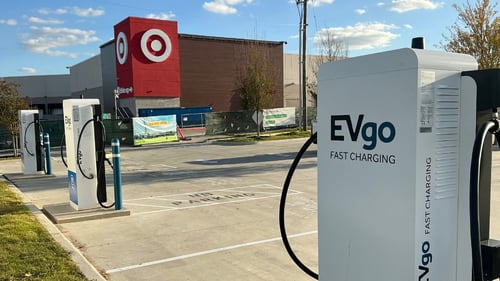 Several EVgo fast-charging units installed in marked parking spaces at a public charging station, with EVgo logos on the chargers, protective bollards around each unit