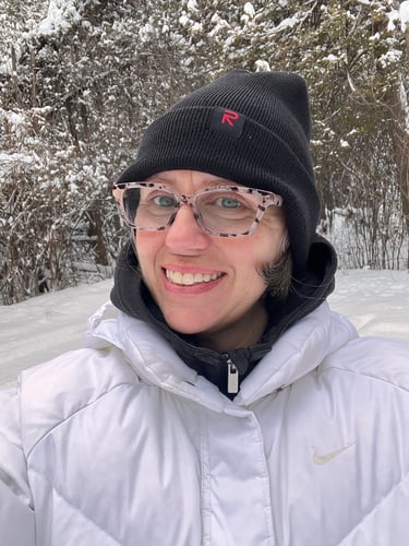 Selfie of Colleen wearing a beanie and a coat with a snowy landscape in the background