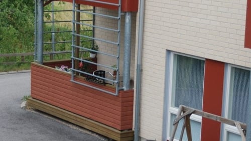 Ulkokuva Kiikkaistentiestä. Rakennus on vaaleaa tiiltä, ka siinä punaisia yksityiskohtia. Pihalla on keinutuoli ja neljä korituolia.
