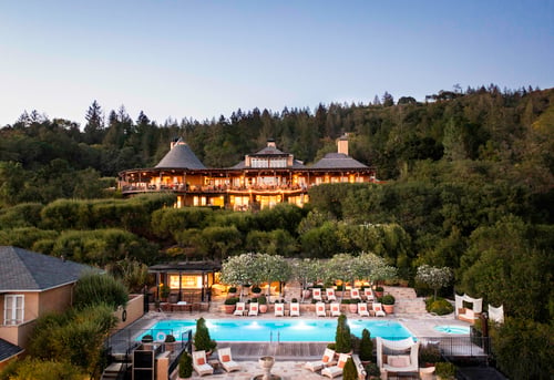 Hillside resort among the trees overlooking a pool at dusk.