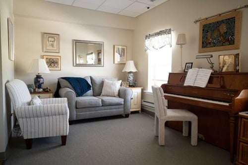 Cozy senior living room with piano, armchairs, and natural light.
