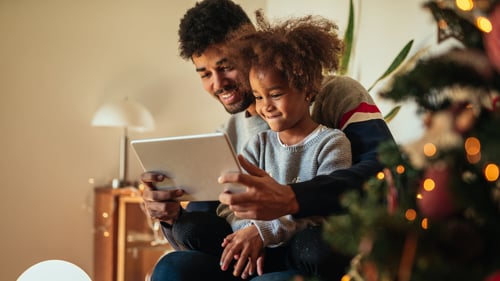 Dad and daughters sitting next to a Christmas Tree.