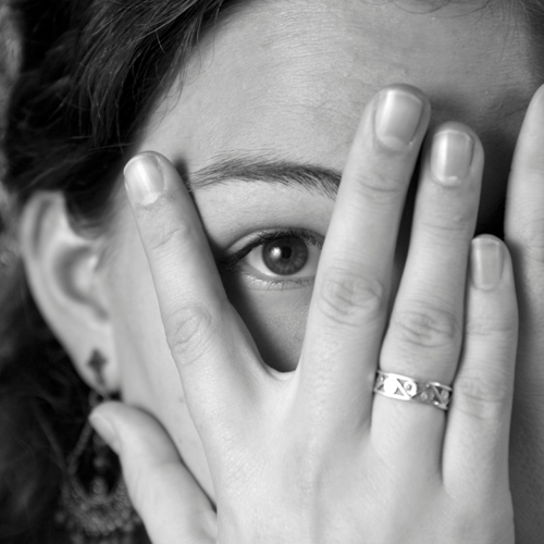 A woman covering her face with a small space for her eye to see.