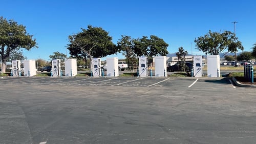 Several EVgo fast-charging units installed in marked parking spaces at a public charging station, with EVgo logos on the chargers, protective bollards around each unit
